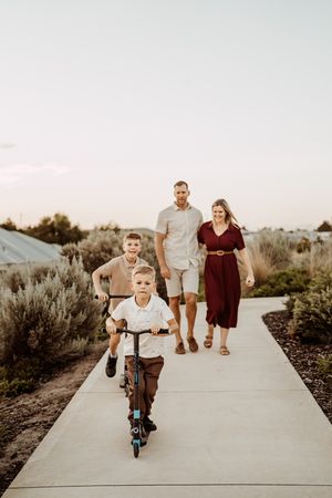 Parents follow joyfully behind small child riding scooter on desert path during sunset photo shoot.