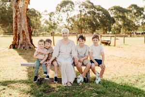 Family members sit together on grass near a large tree trunk during an outdoor photo session.