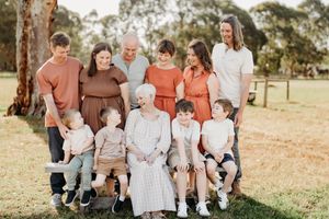 A multi-generational family group poses together outdoors wearing coordinated autumn-toned casual clothing.