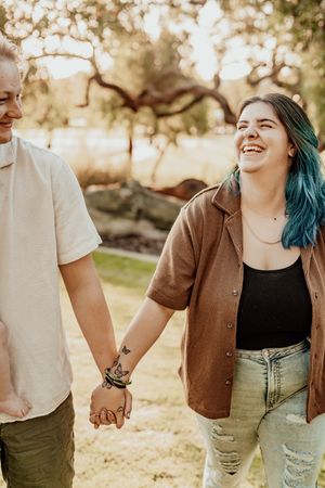 Happy couple holding hands and laughing together in a sun-drenched outdoor setting with natural bokeh effects.