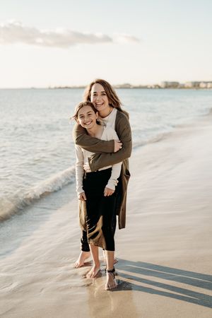 Couple enjoying playful moments on a serene beach during sunset with soft waves in the background.
