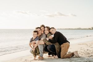 A loving family poses together on a sandy beach at sunset with ocean waves in the background.