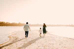 A family walks together along a sunlit sandy beach during golden hour on a calm peaceful day.