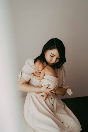 Parent and baby share a tender moment in matching cream-colored outfits against minimal background.