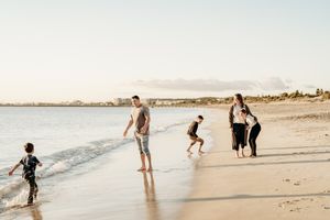 People walk and play along a serene beach shoreline during golden hour with mountains visible in the distance.