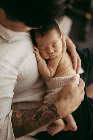 A sleeping newborn being cradled in arms with a distinctive floral tattoo sleeve visible.