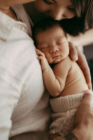 A sleeping baby lies peacefully against soft white bedding while wearing a cozy knit sweater in a tender close-up photograph.