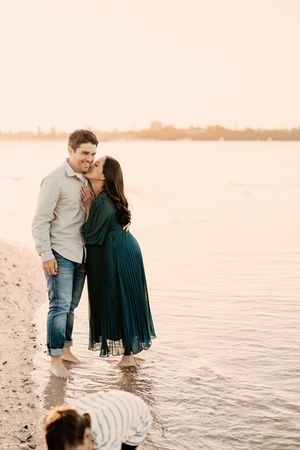 A couple shares an intimate moment on the beach at sunset while their dog plays in the water.