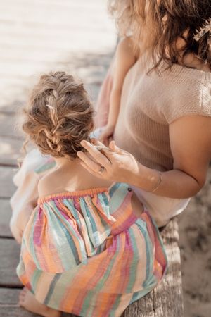 Someone braids colorful stripes summer dress on beach at sunset with soft dreamy lighting effect.