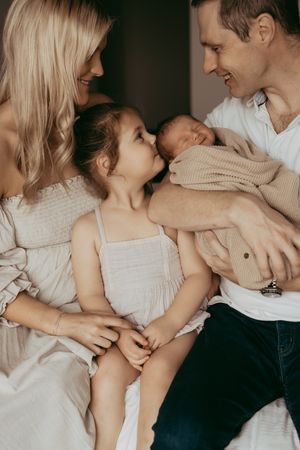 Family of four wearing light colored clothing gather close together in an intimate portrait at home.