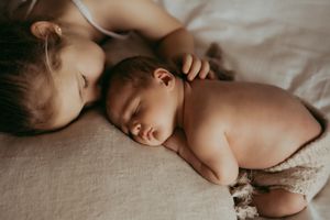 Two babies sleeping peacefully together on soft white bedding in warm natural light.
