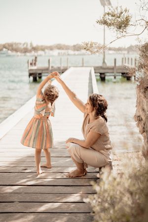 Sweet moment of dancing together on a wooden pier by the water in soft vintage tones.