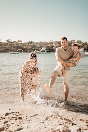 A romantic couple plays and splashes in the ocean water at sunset, creating joyful moments at the beach.