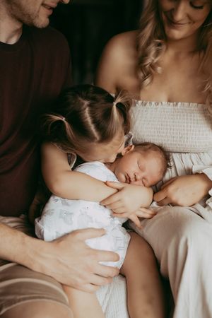 Intimate family portrait shows tender moment with sleeping newborn baby being cradled and kissed.