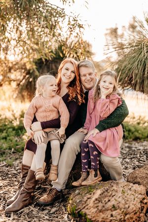 A family in coordinated outfits sits together on a rock during golden hour at a park.