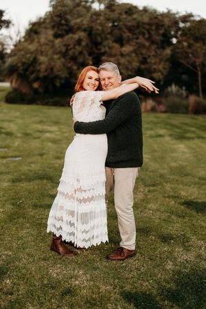 A couple embraces joyfully on a green lawn during their engagement photoshoot session.