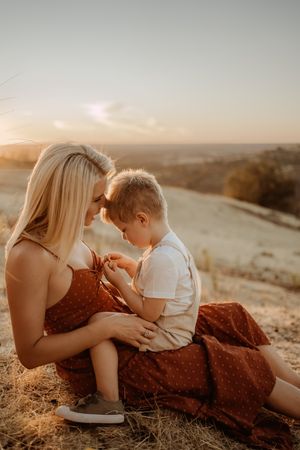 A tender sunset moment captured between parent and child sitting on a hillside in golden evening light.