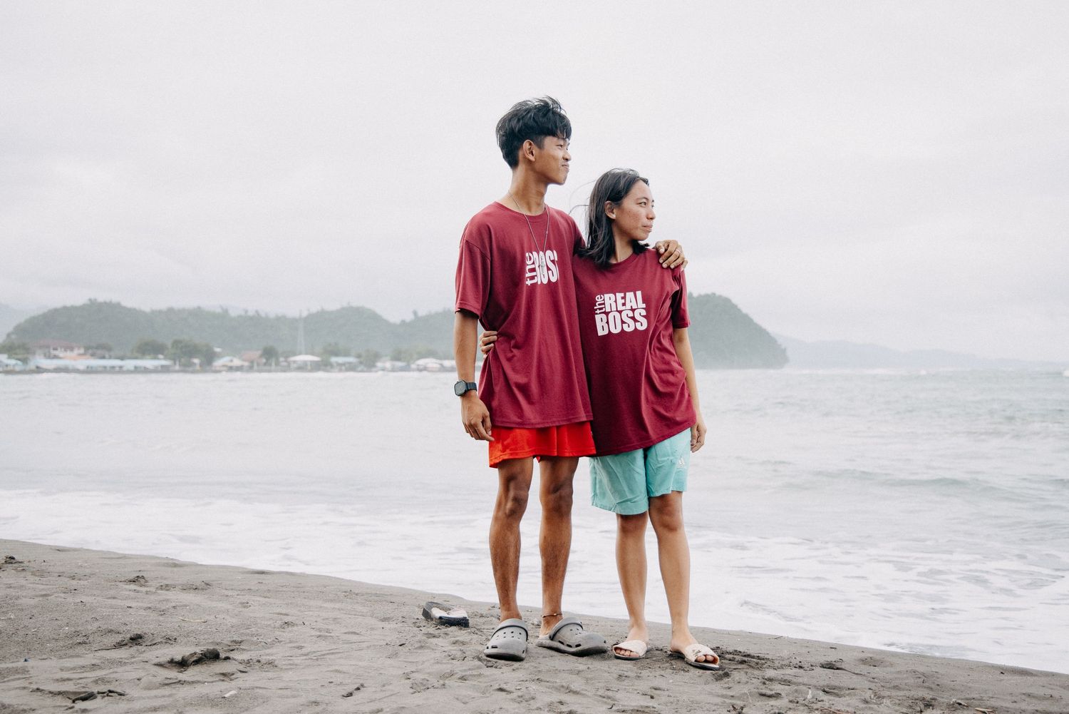 Children in casual clothes standing together on a beach with mountains in the background.