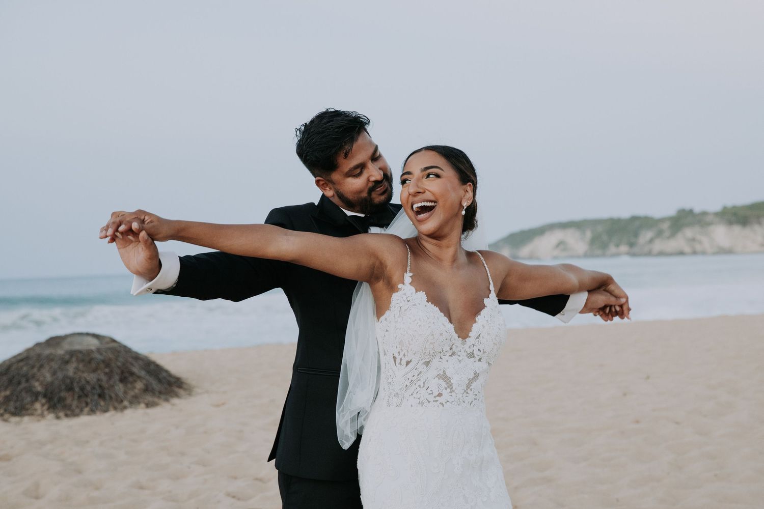 A romantic couple embraces on a sandy beach during an outdoor photo session.