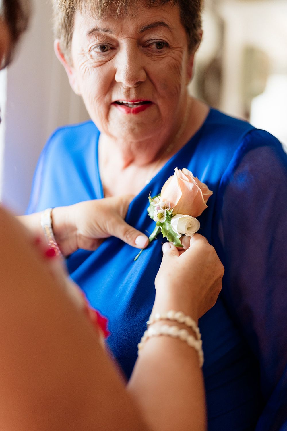 Person wearing a blue shirt and bracelets enjoys a small sandwich while sitting indoors.