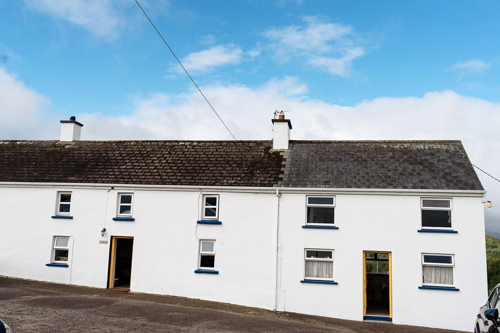 Traditional Irish white cottage with two entrances and multiple windows under a gray tiled roof against blue sky.