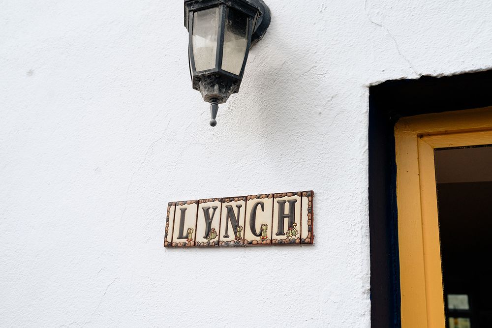 A rustic wooden 'LUNCH' sign mounted on a white wall next to a yellow door and vintage lantern.