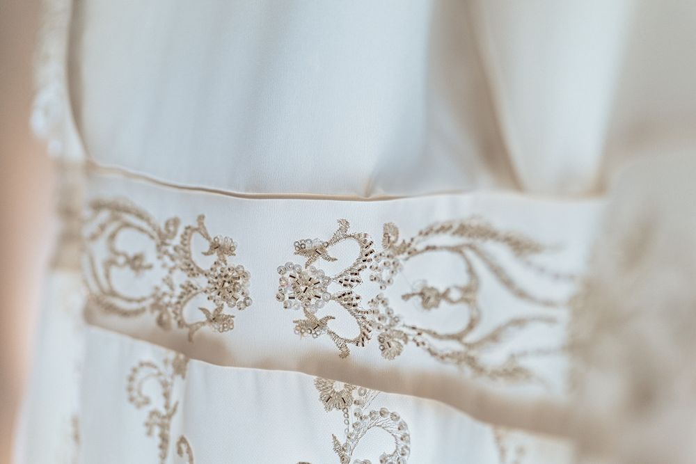 Close up detail of delicate lace embroidery and beading on white wedding dress fabric.