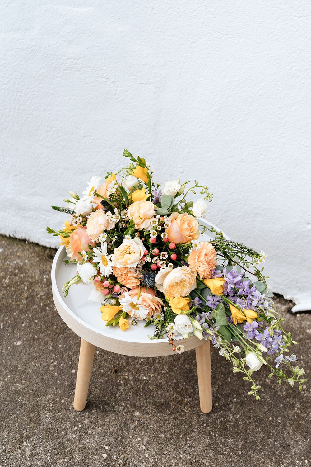 A stunning peach and purple floral arrangement with roses and greenery displayed on a small white round table.