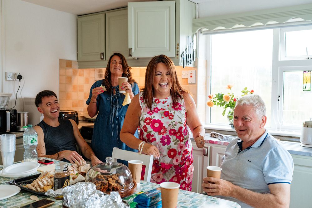 A festive gathering of people enjoying food and drinks in a bright kitchen with white cabinets.