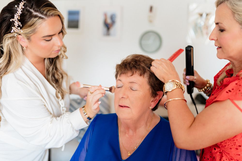 Two stylists working together to apply makeup and style hair in bright white room with professional salon setup.