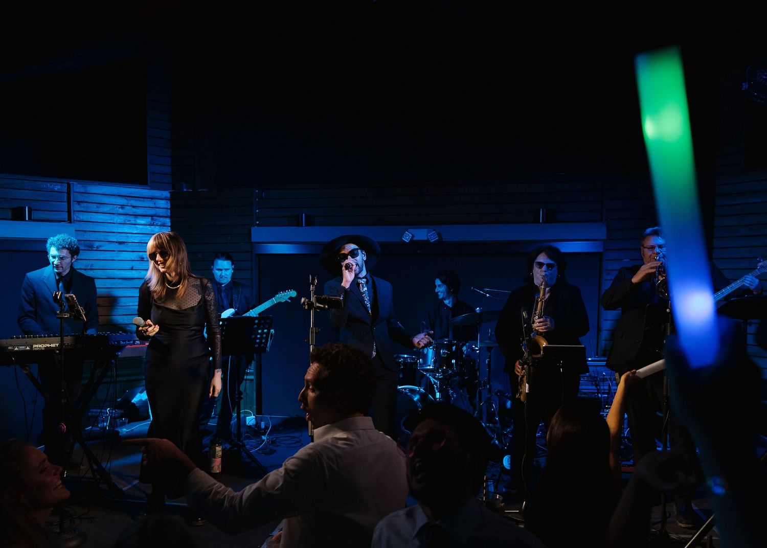 A live band performs on a dimly lit stage with blue lighting for a wedding reception crowd.