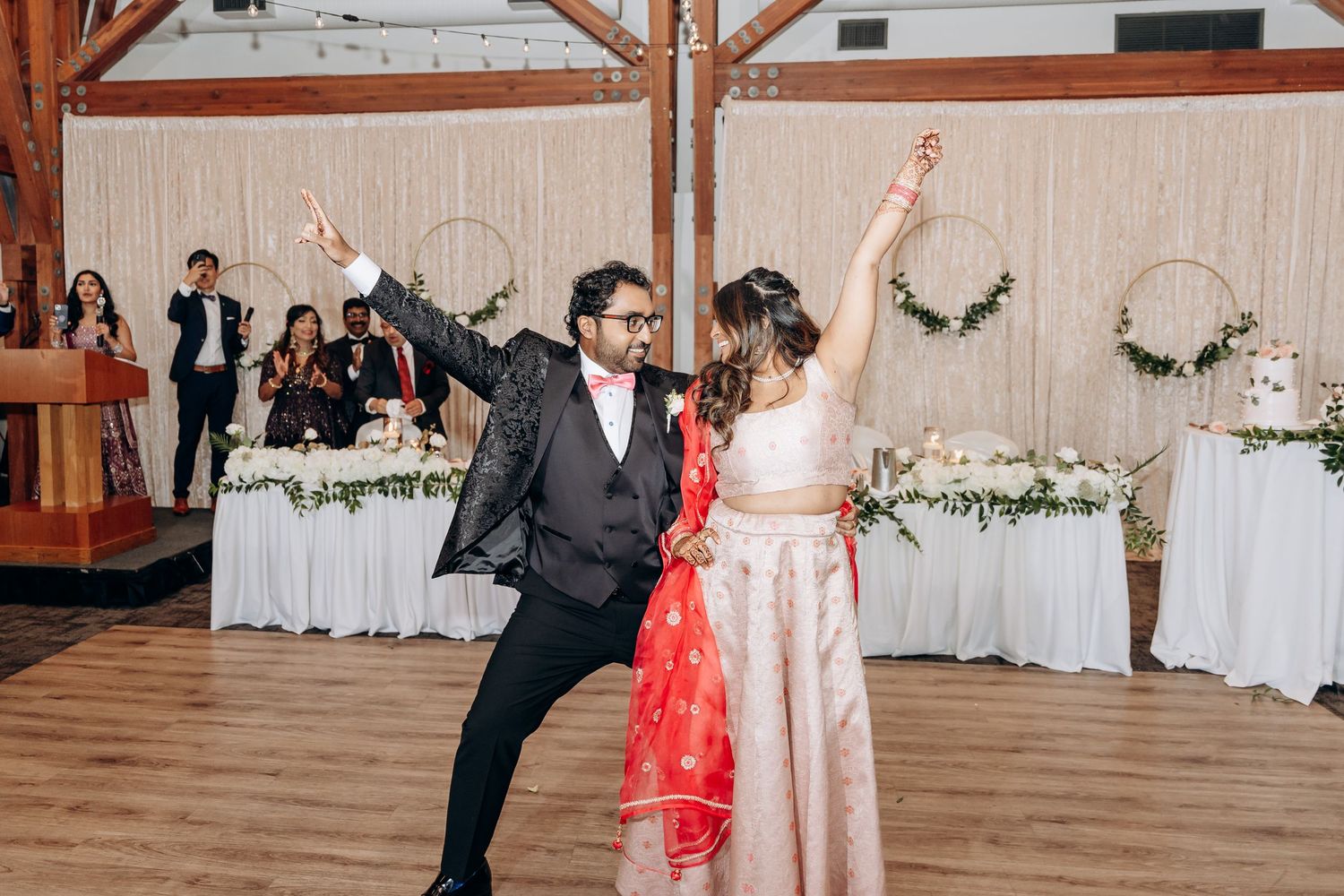 Wedding reception celebration in a rustic wooden venue with decorative white drapes and lighting.