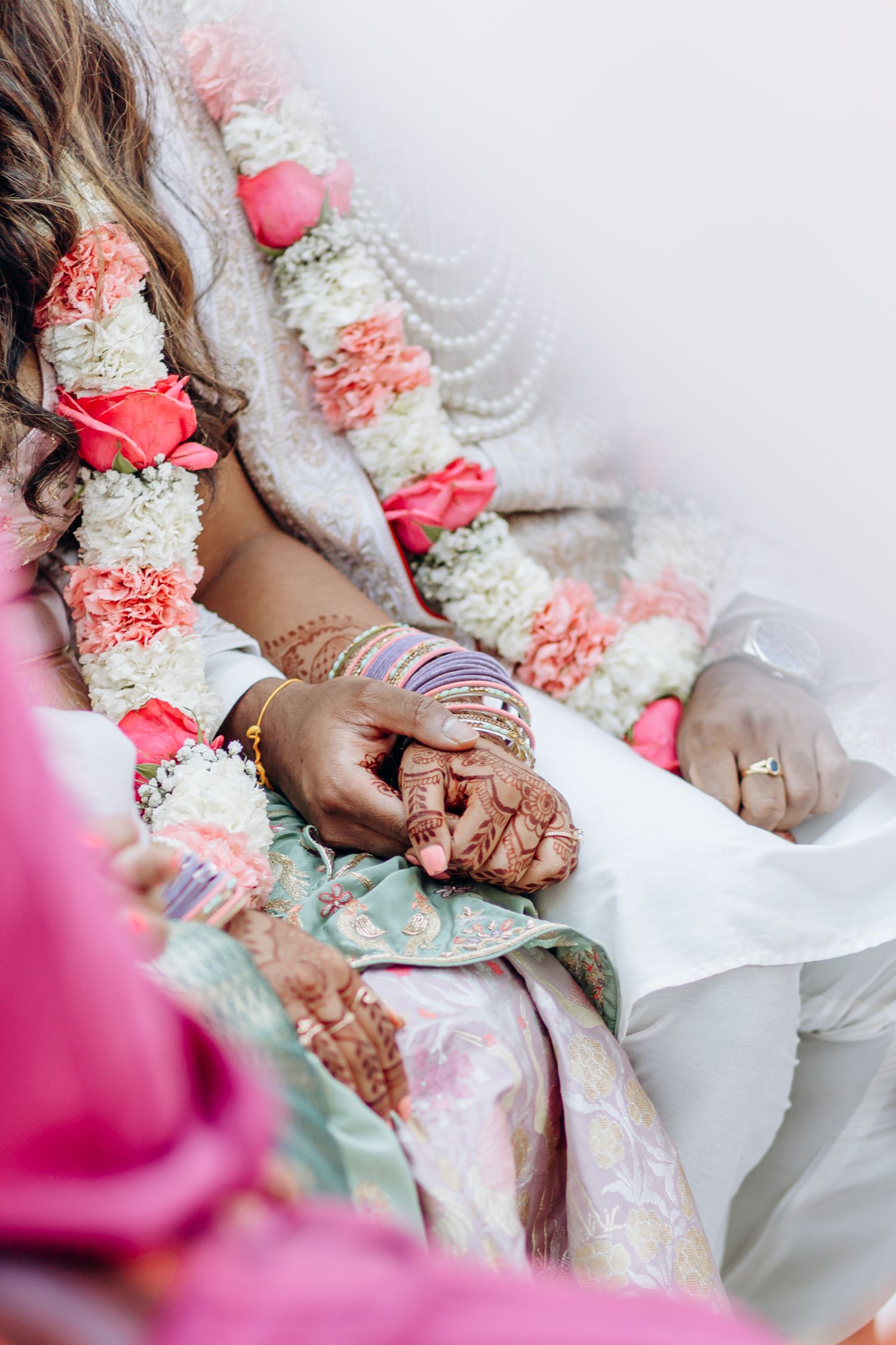 Close-up of hands adorned with traditional henna designs and jewelry against white fabric.