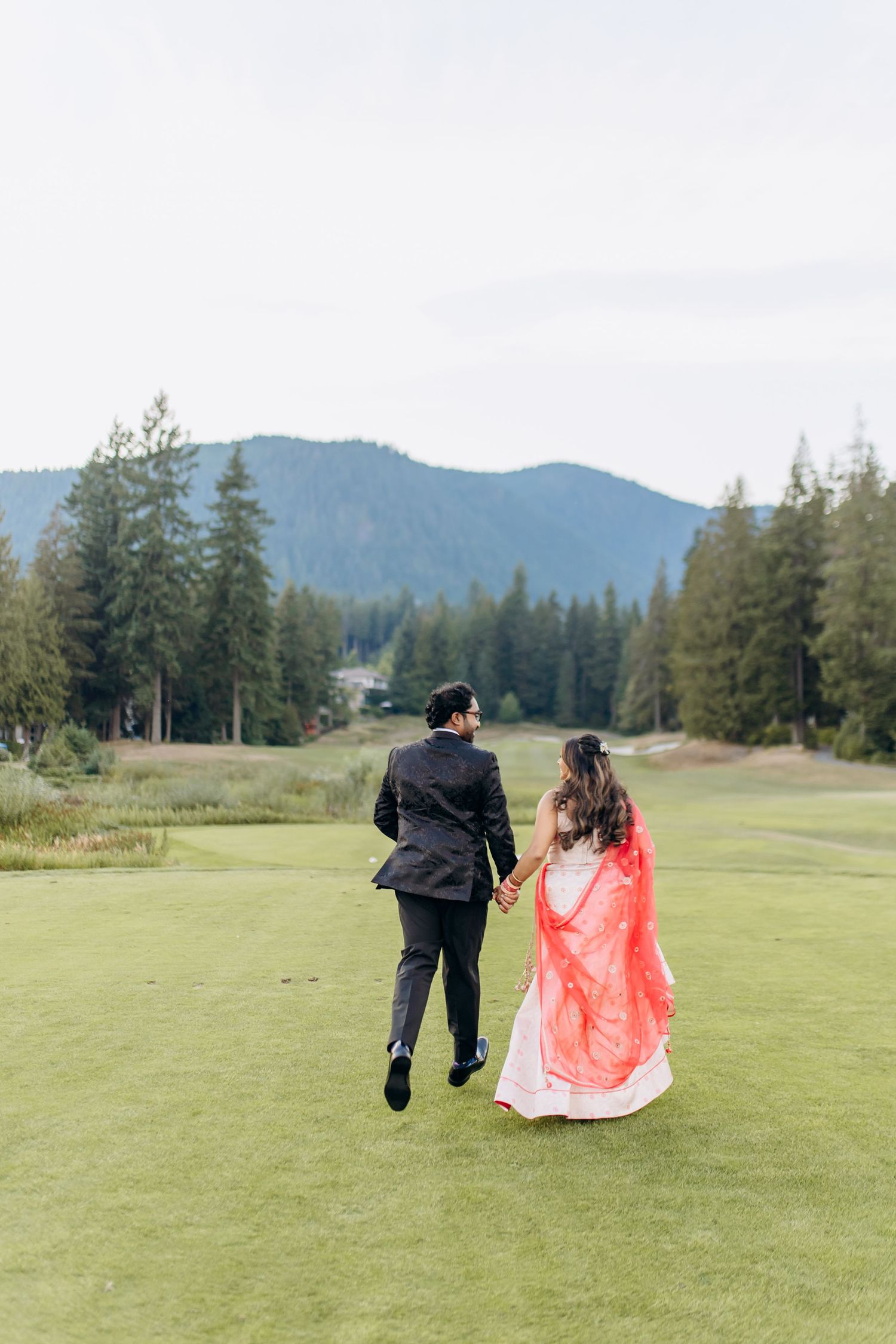 Couple walking across a scenic golf course with mountains and evergreen trees in the background.