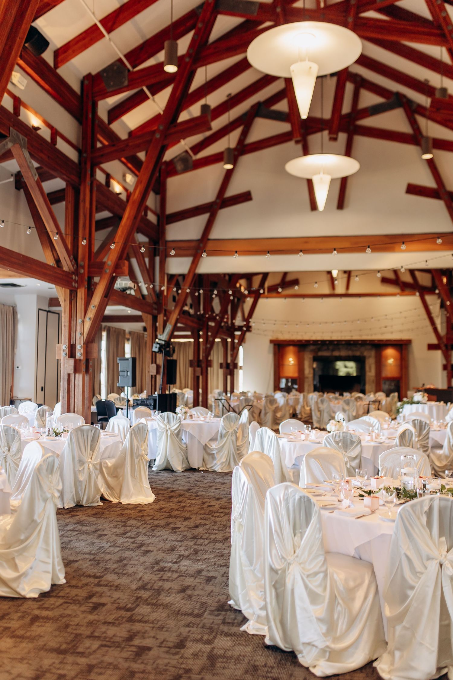 Spacious wedding reception hall with exposed wooden beams and tables dressed in white linens.