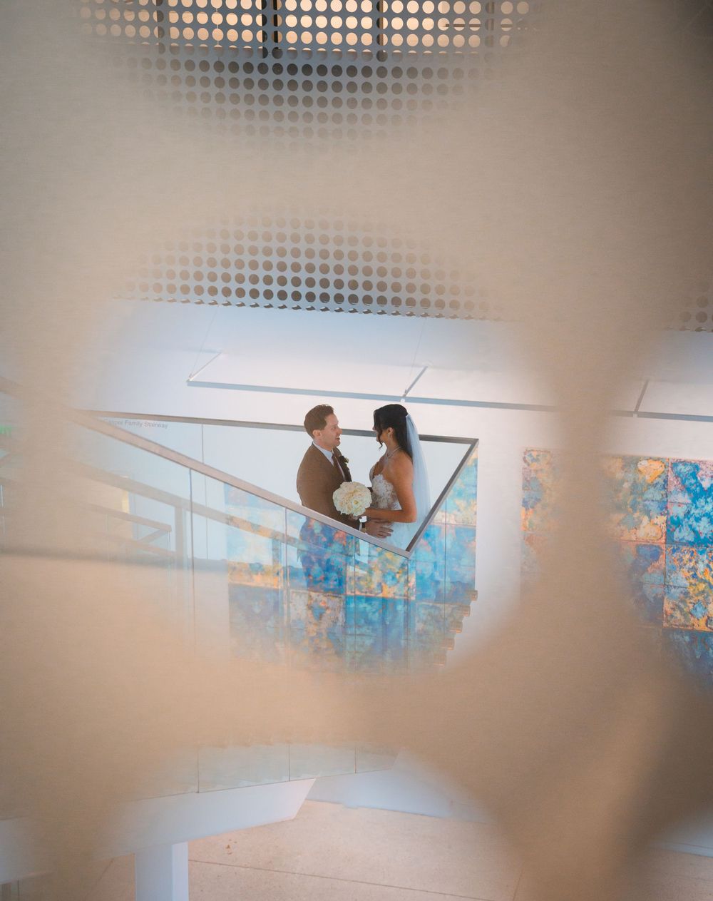 A couple shares an intimate moment on a balcony overlooking blue decor elements, viewed through a blurred circular pattern.