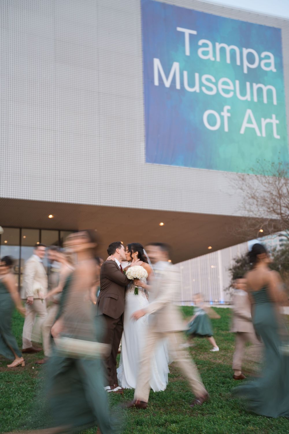 Motion-blurred group dancing at outdoor wedding reception near Tampa Museum of Art building sign at dusk.