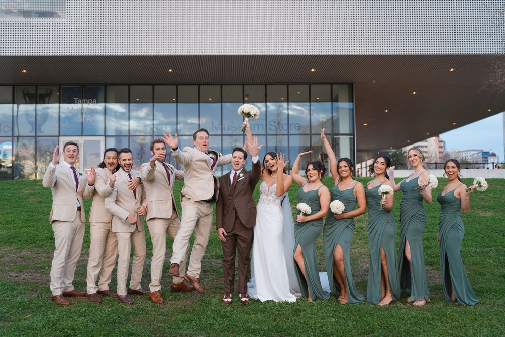 Wedding party poses together on grass with the couple in center and attendants wearing tan suits and green dresses.