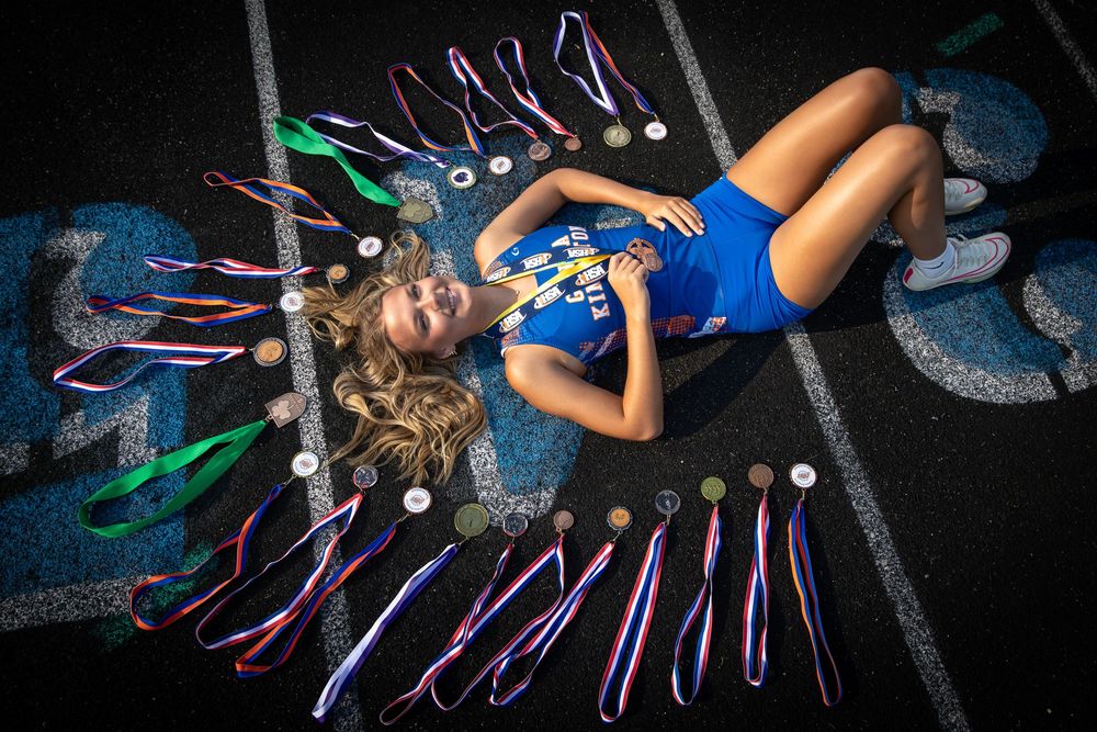 Young athlete lying on track surrounded by medals and ribbons, celebrating sports achievements in blue uniform.
