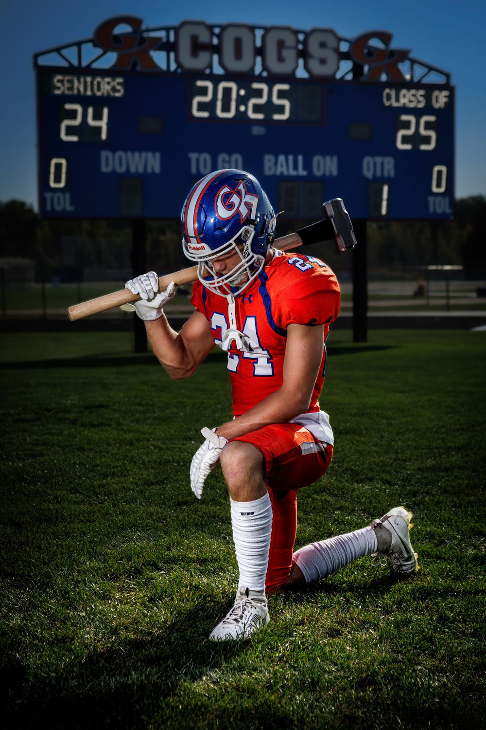 Football player in orange uniform and helmet performs athletic stance on grass field.