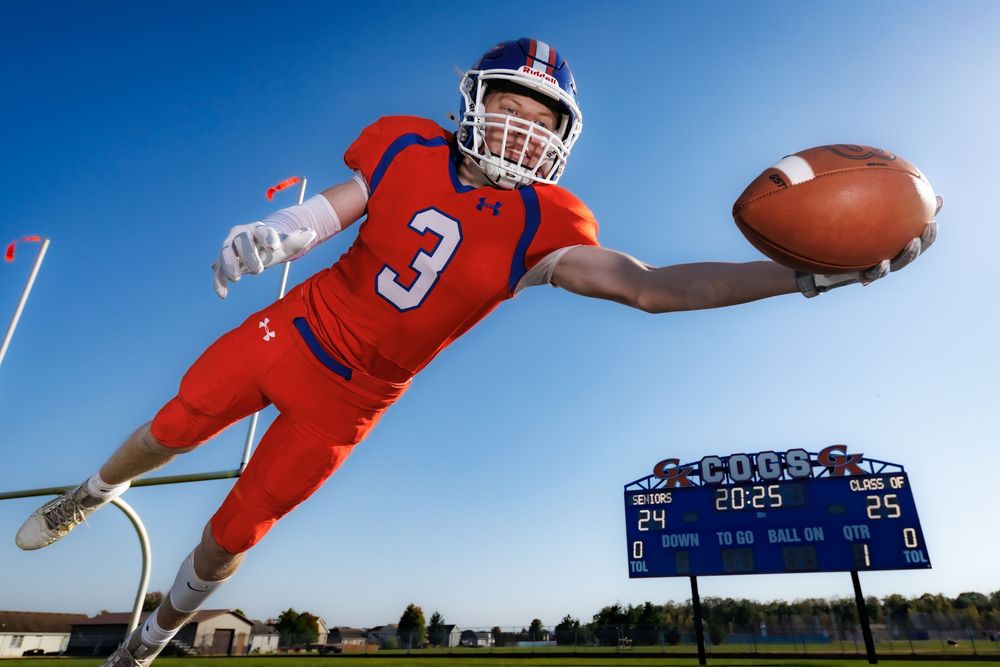 Dynamic action shot of football player diving to catch ball against blue sky.