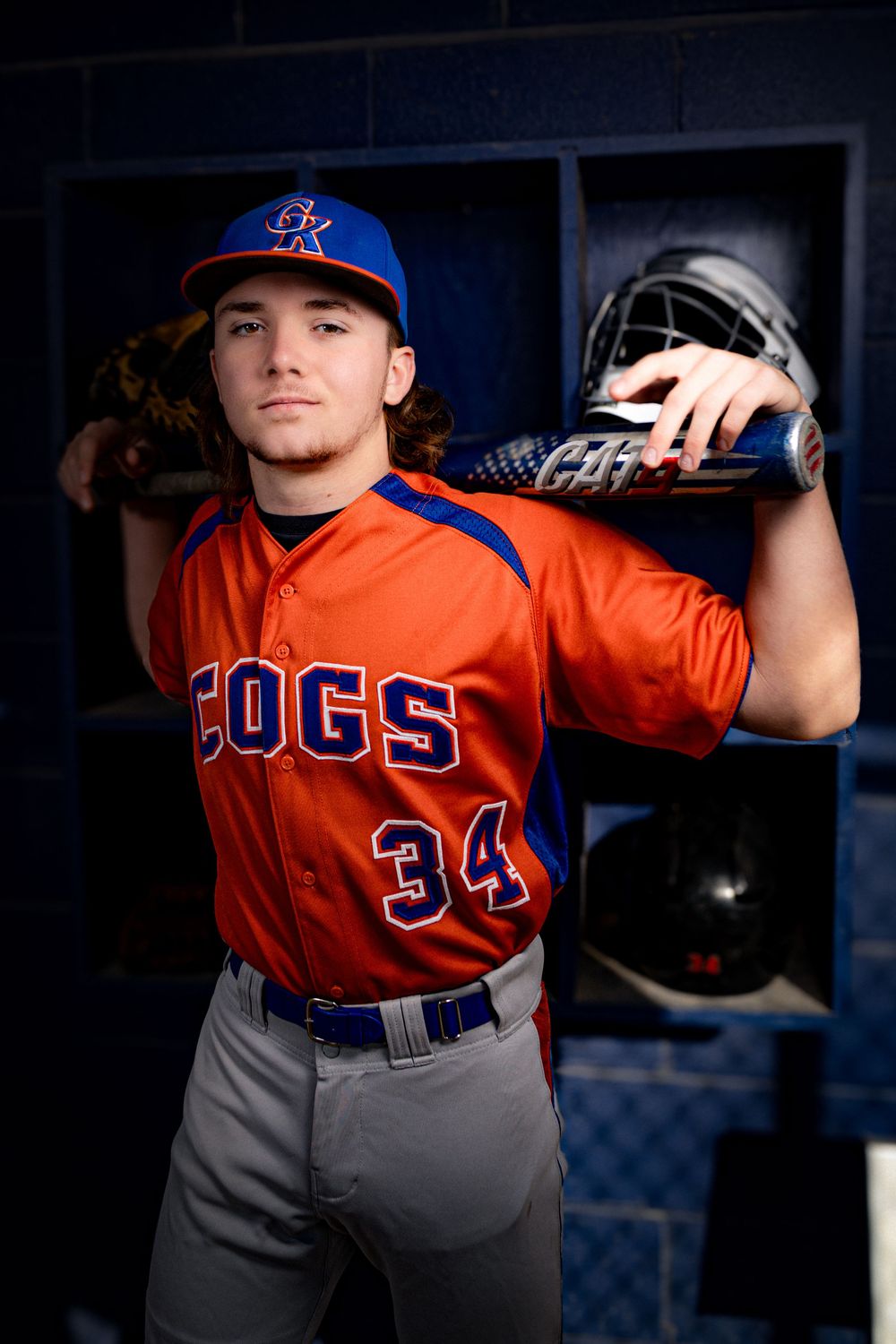 Baseball player in orange and blue uniform posing in dugout for dramatic sports portrait.