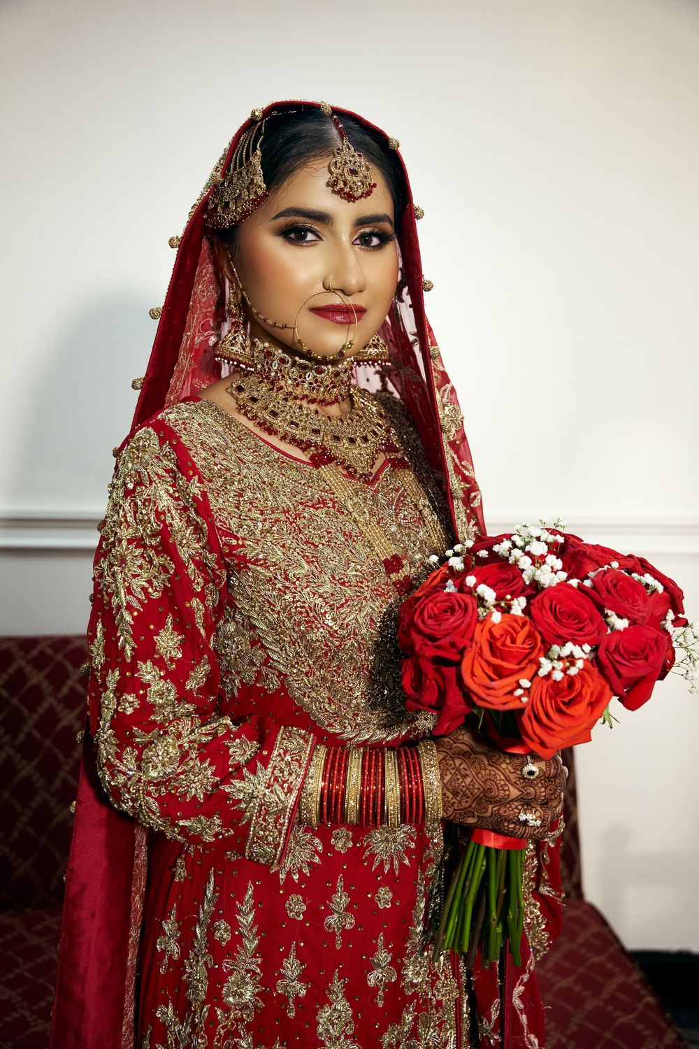 Traditional South Asian bridal attire in red and gold embroidery paired with a bouquet of red roses at Antuns by Minar