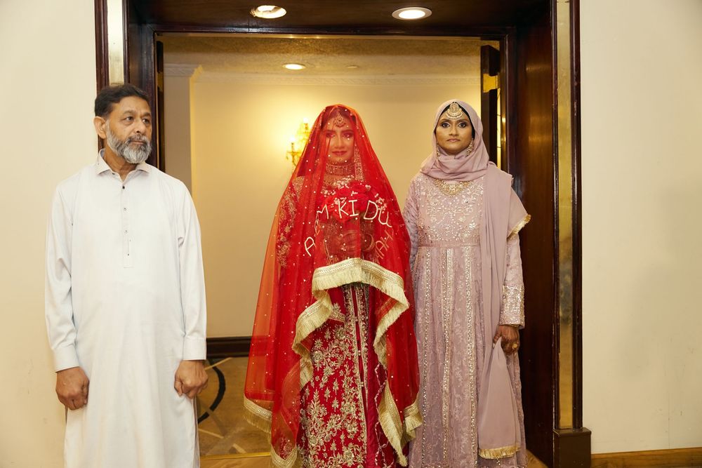 Three people in traditional South Asian attire stand by a doorway, including a bride in an ornate red and gold dress. at Antuns by Minar