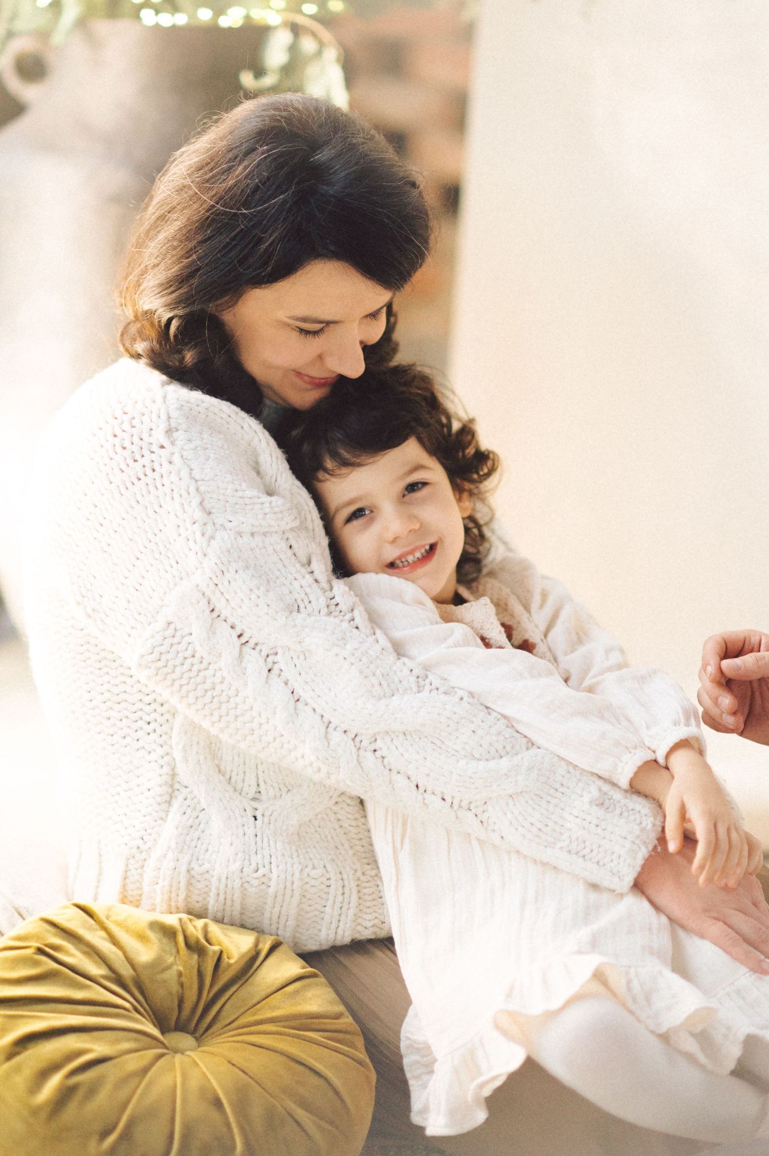 A warm and intimate moment as two figures in white clothing share a loving embrace beside a gold velvet cushion.