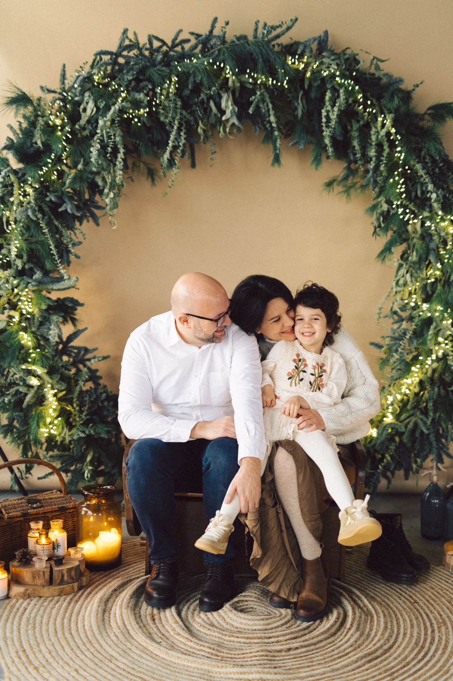 A sweet family photo session with evergreen garland decorations and a circular rug on a beige background.