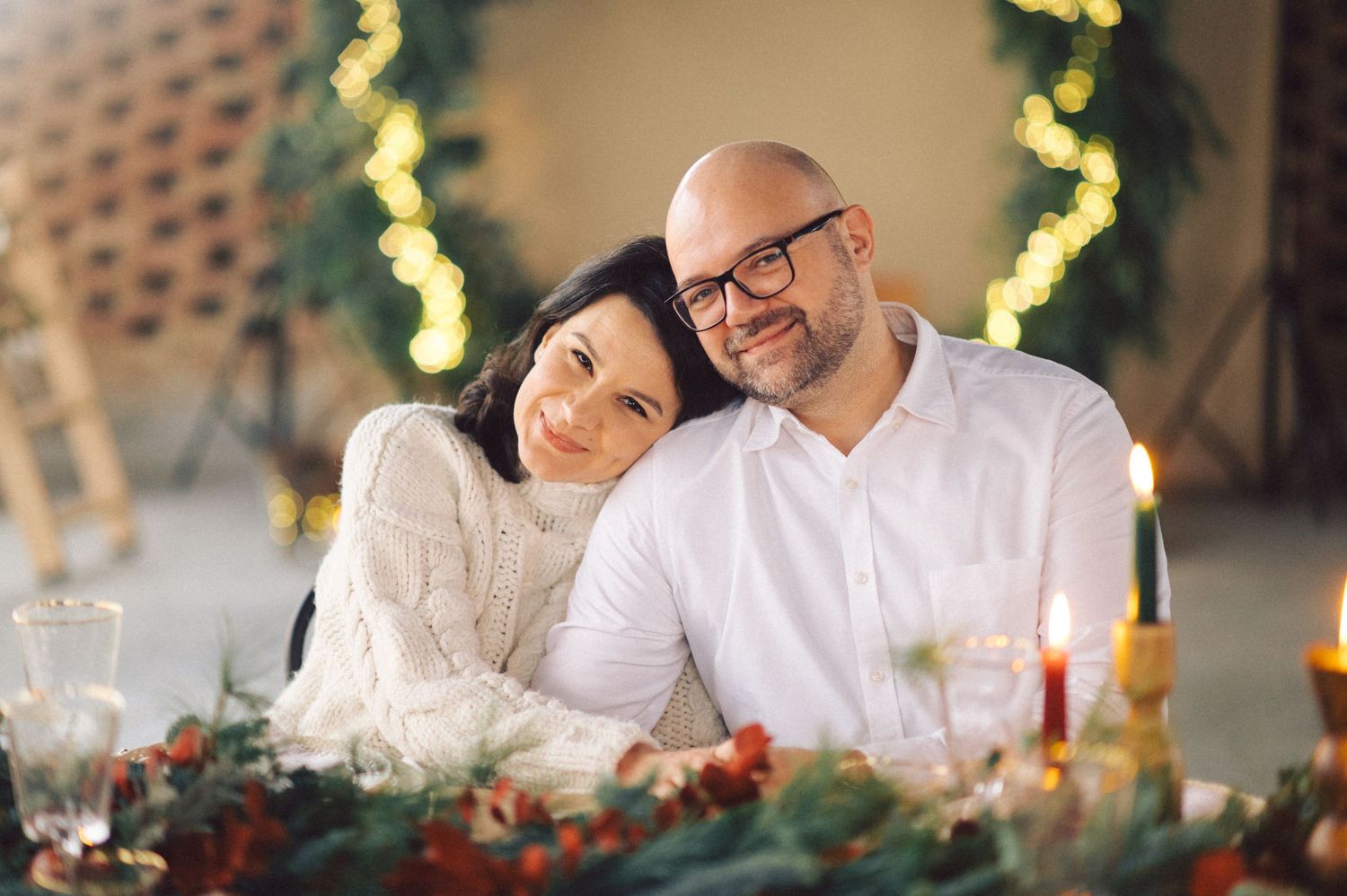 Happy couple enjoying romantic dinner date at restaurant with festive holiday decorations visible in background.