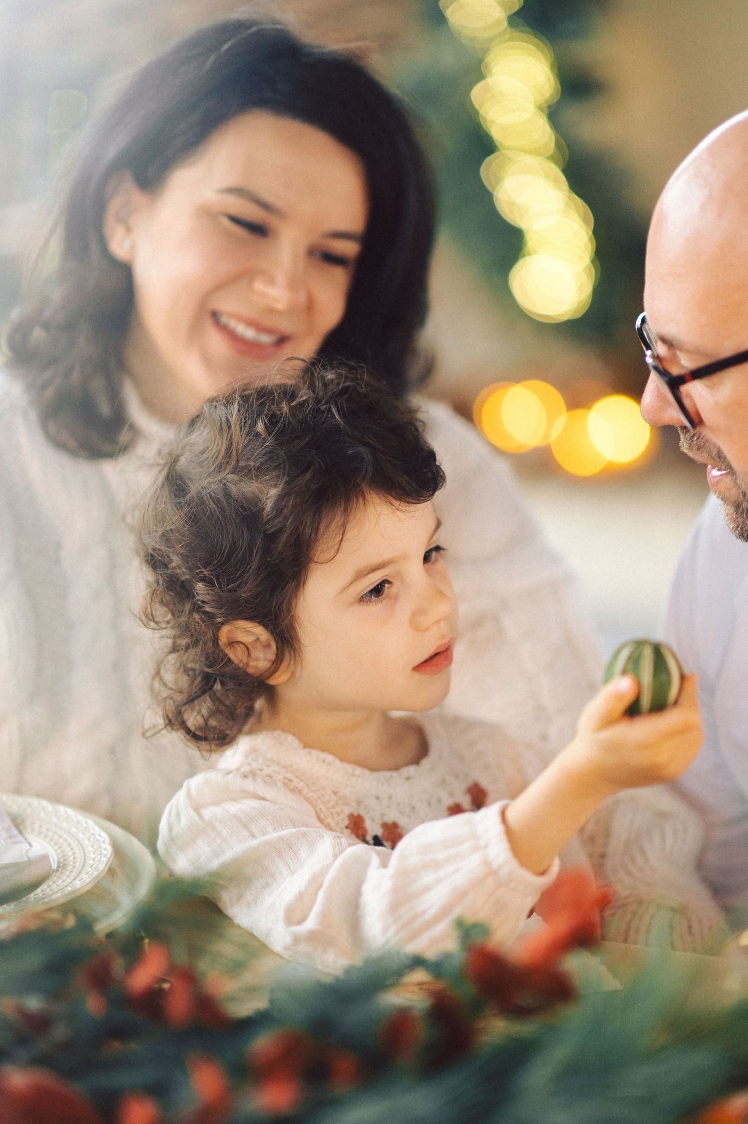 Family sharing a joyful holiday moment as they decorate with Christmas ornaments and evergreen branches.