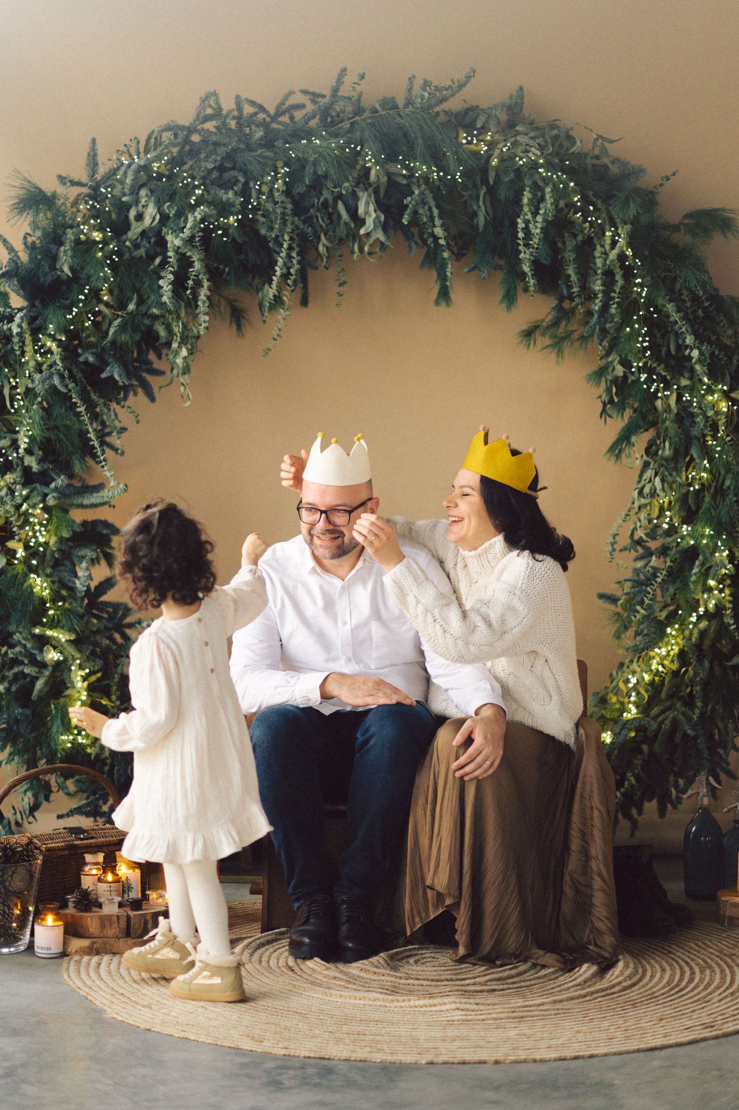 Progressive sequence showing a casual family photoshoot with eucalyptus garland decorations on a beige backdrop.
