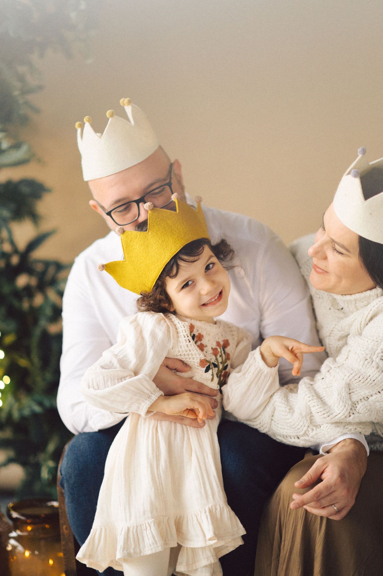 Four connected images show sweet moments with a small child in a white dress and gold crown playing in warm lighting.